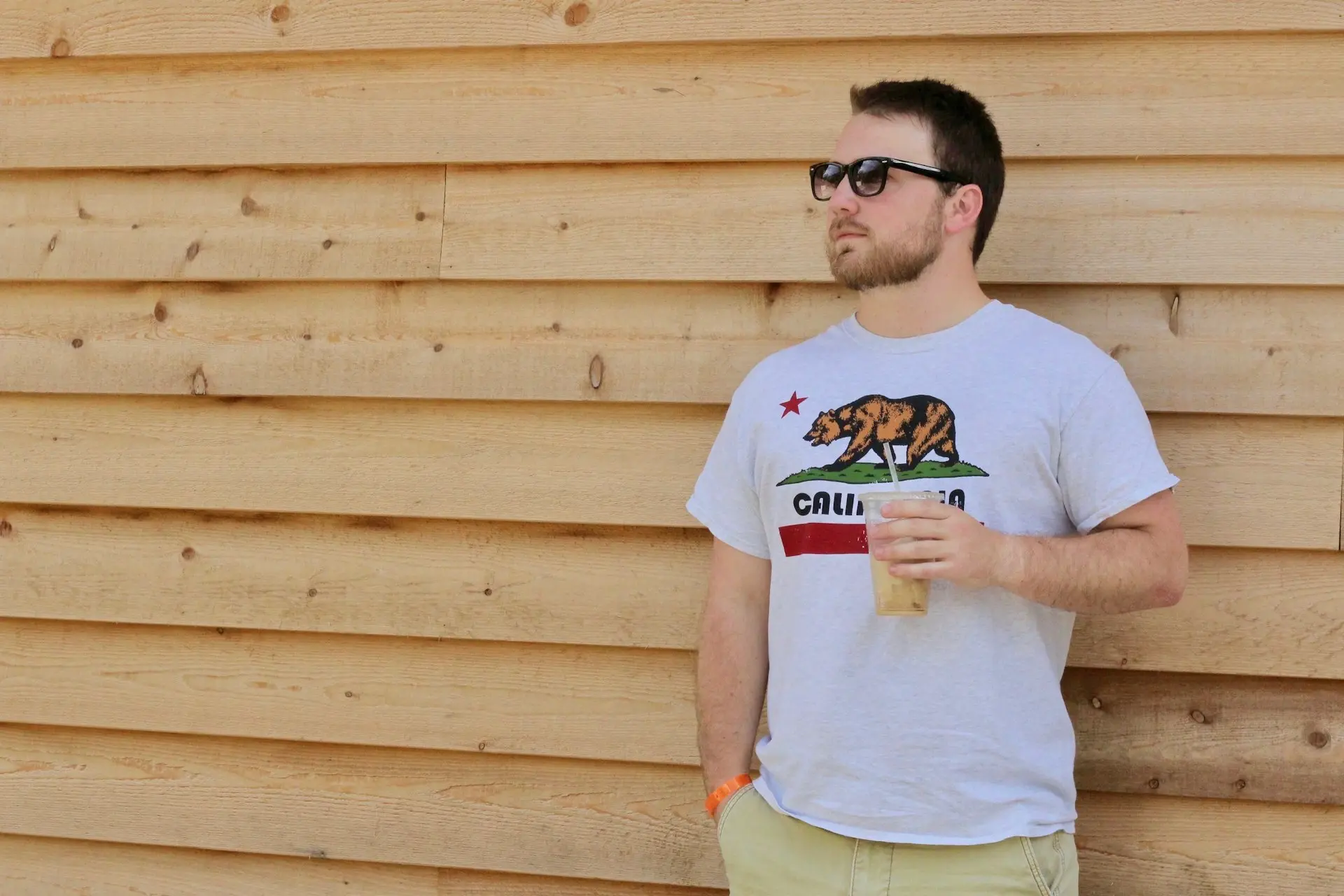 man wearing eyeglasses holding plastic cup standing in front of brown wall